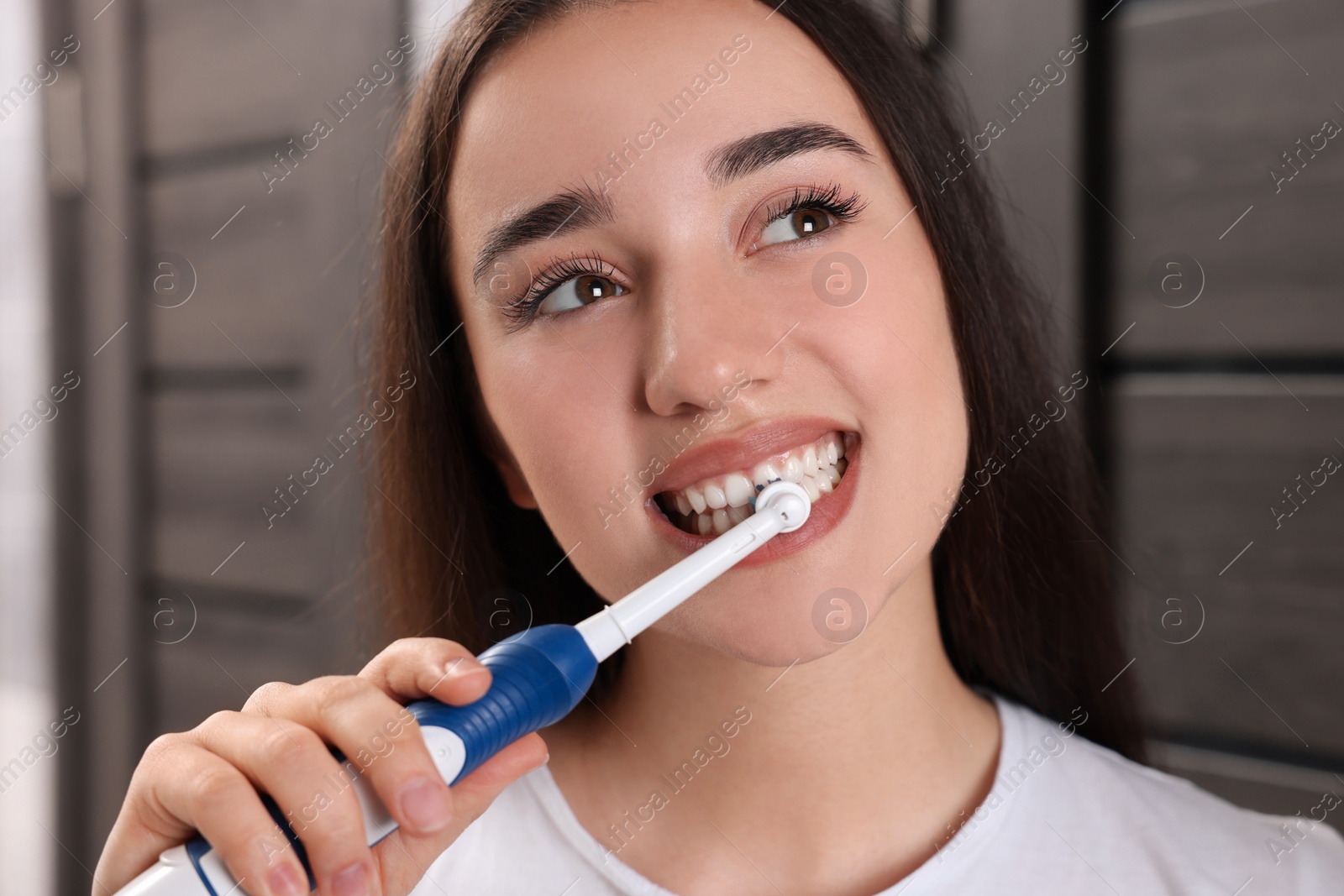 Photo of Woman brushing her teeth with electric toothbrush in bathroom, closeup