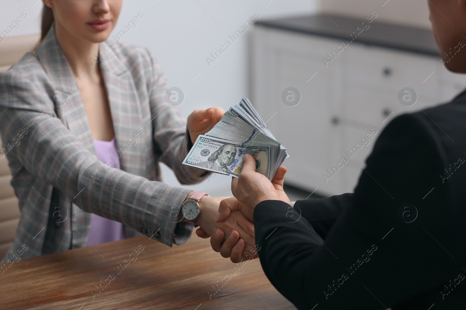 Photo of Man shaking hands with woman and offering bribe at table indoors, closeup