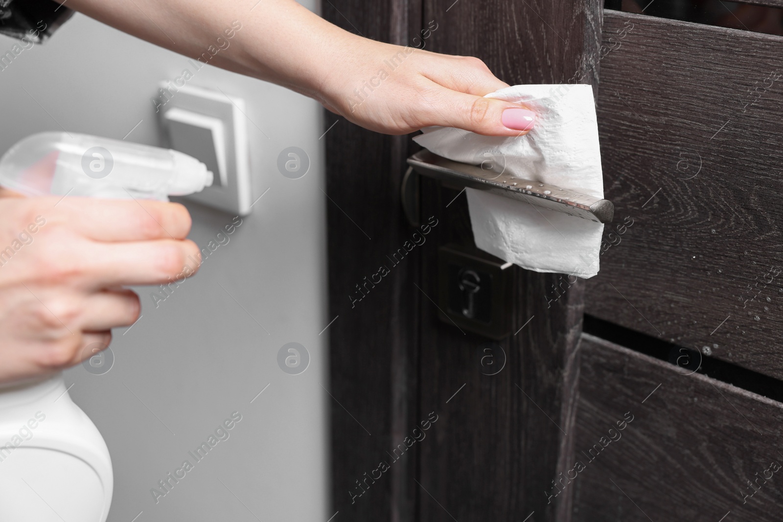 Photo of Woman cleaning door handle with detergent and paper towel, closeup