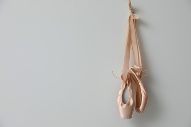 Beautiful beige ballet shoes with cute ribbons hanging on light grey wall. Space for text