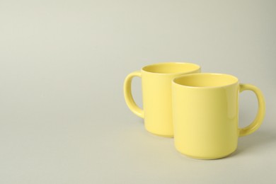 Two yellow ceramic mugs on light grey background, space for text