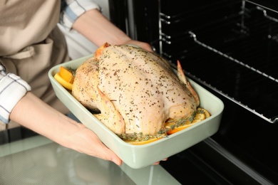 Photo of Woman putting raw chicken with orange slices into oven, closeup