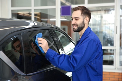 Photo of Worker cleaning automobile window with rag at car wash