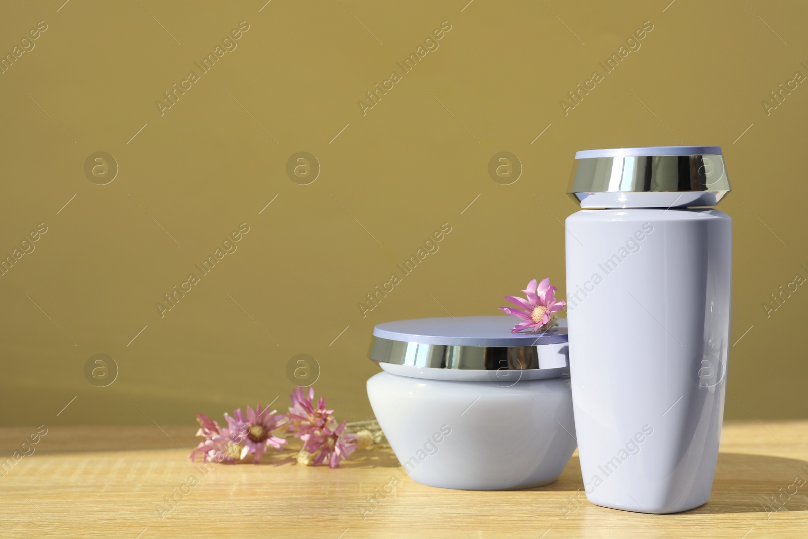 Photo of Hair care cosmetic products and beautiful flowers on wooden table, space for text