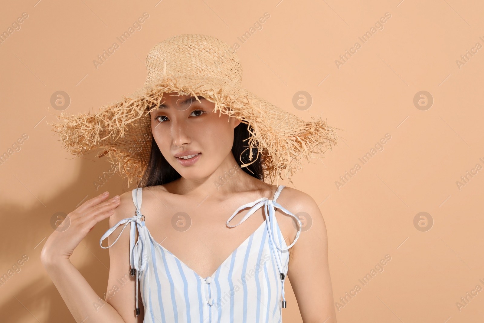 Photo of Beautiful young woman in straw hat on beige background, space for text