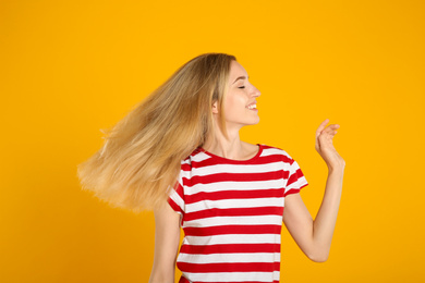 Portrait of beautiful young woman with blonde hair on yellow background