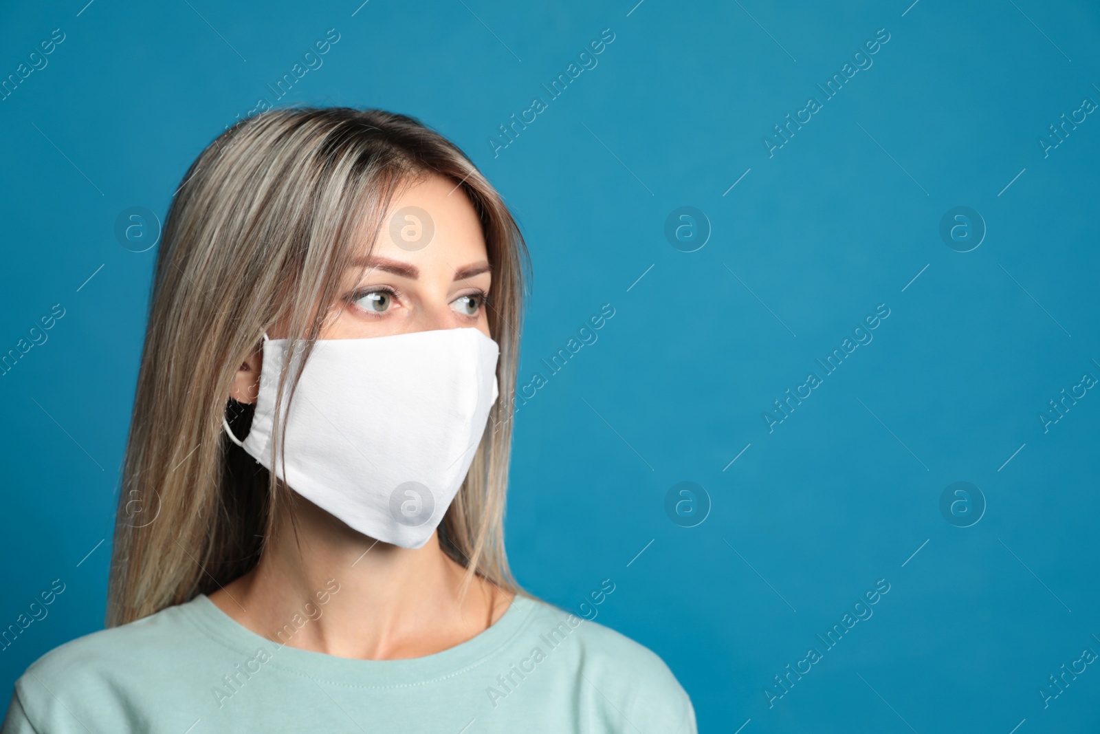 Photo of Young woman in protective face mask on blue background. Space for text