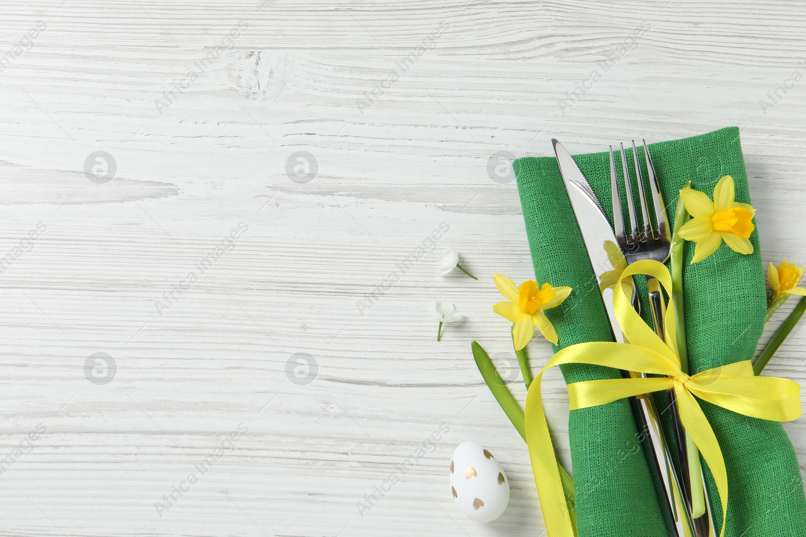 Photo of Cutlery set, Easter egg and narcissuses on white wooden table, flat lay. Space for text