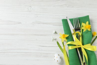 Cutlery set, Easter egg and narcissuses on white wooden table, flat lay. Space for text