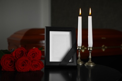 Black photo frame with burning candles and red roses on table in funeral home