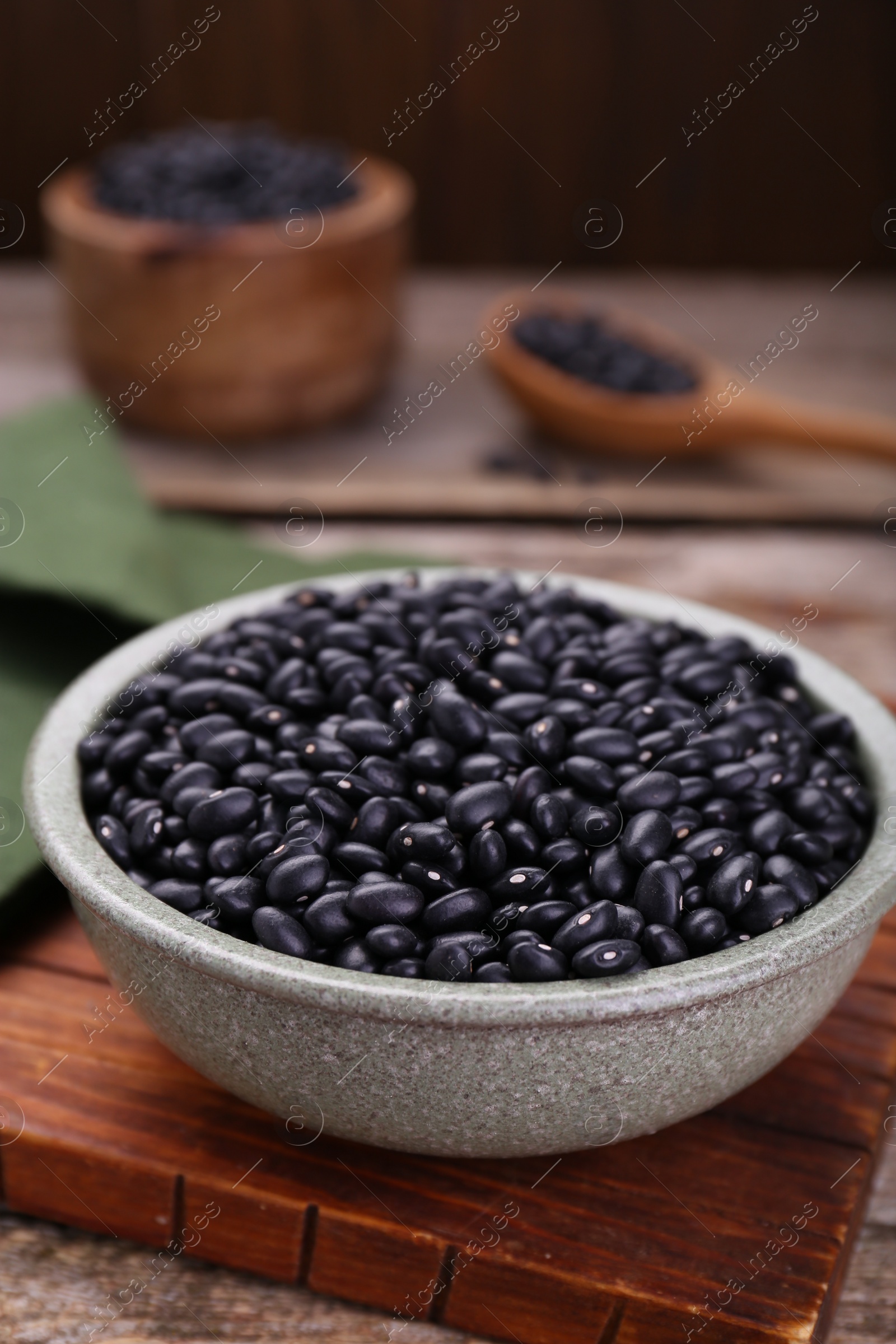 Photo of Bowl of raw black beans on wooden board, closeup
