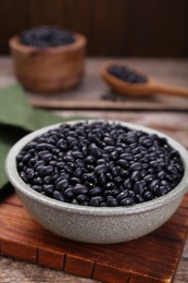 Bowl of raw black beans on wooden board, closeup