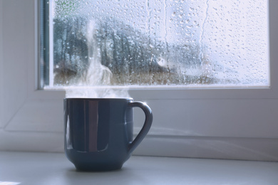 Image of Cup of hot drink near window on rainy day