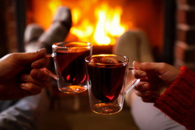 Photo of Couple with tasty mulled wine near fireplace indoors, closeup