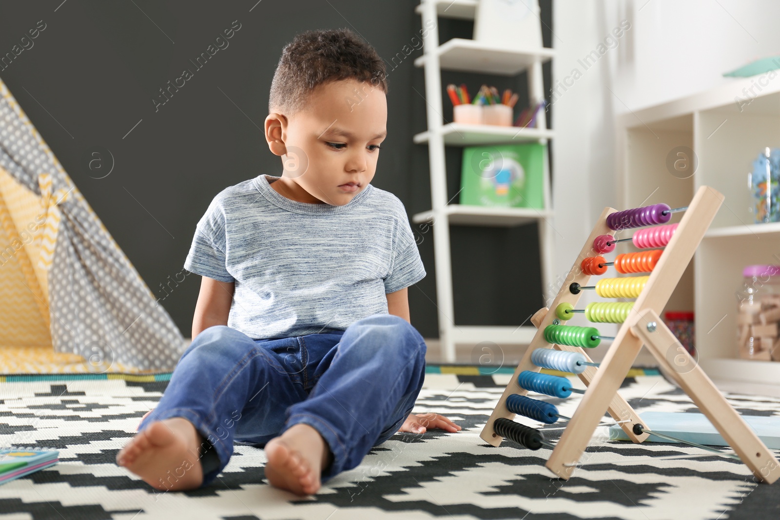 Photo of Cute little African-American child playing with abacus on floor in kindergarten. Indoor activity