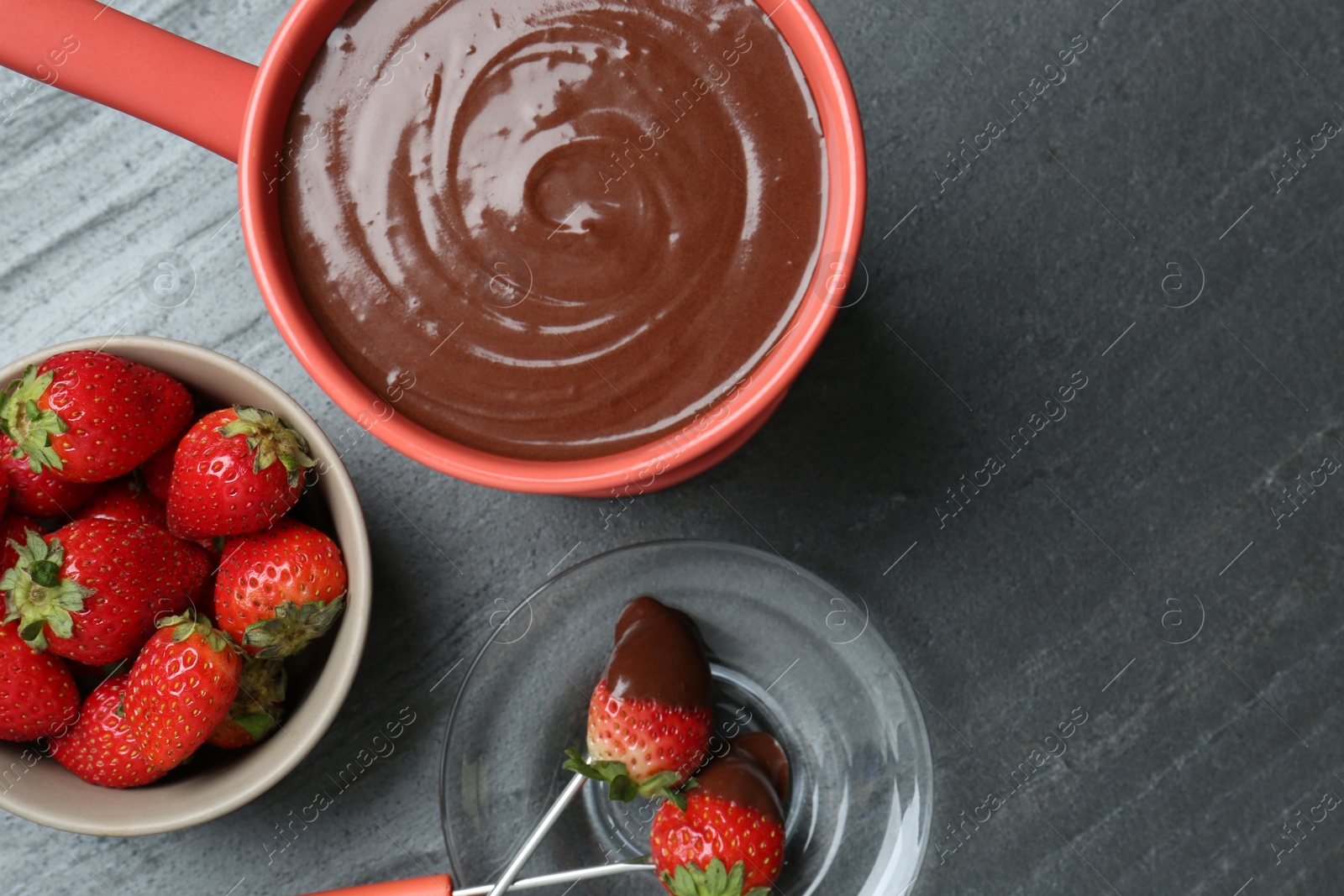 Photo of Fondue pot with melted chocolate, fresh strawberries and forks on grey table, flat lay. Space for text