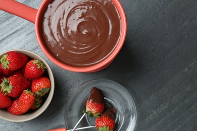 Fondue pot with melted chocolate, fresh strawberries and forks on grey table, flat lay. Space for text