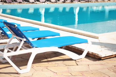 Comfortable loungers at clean swimming pool on sunny day