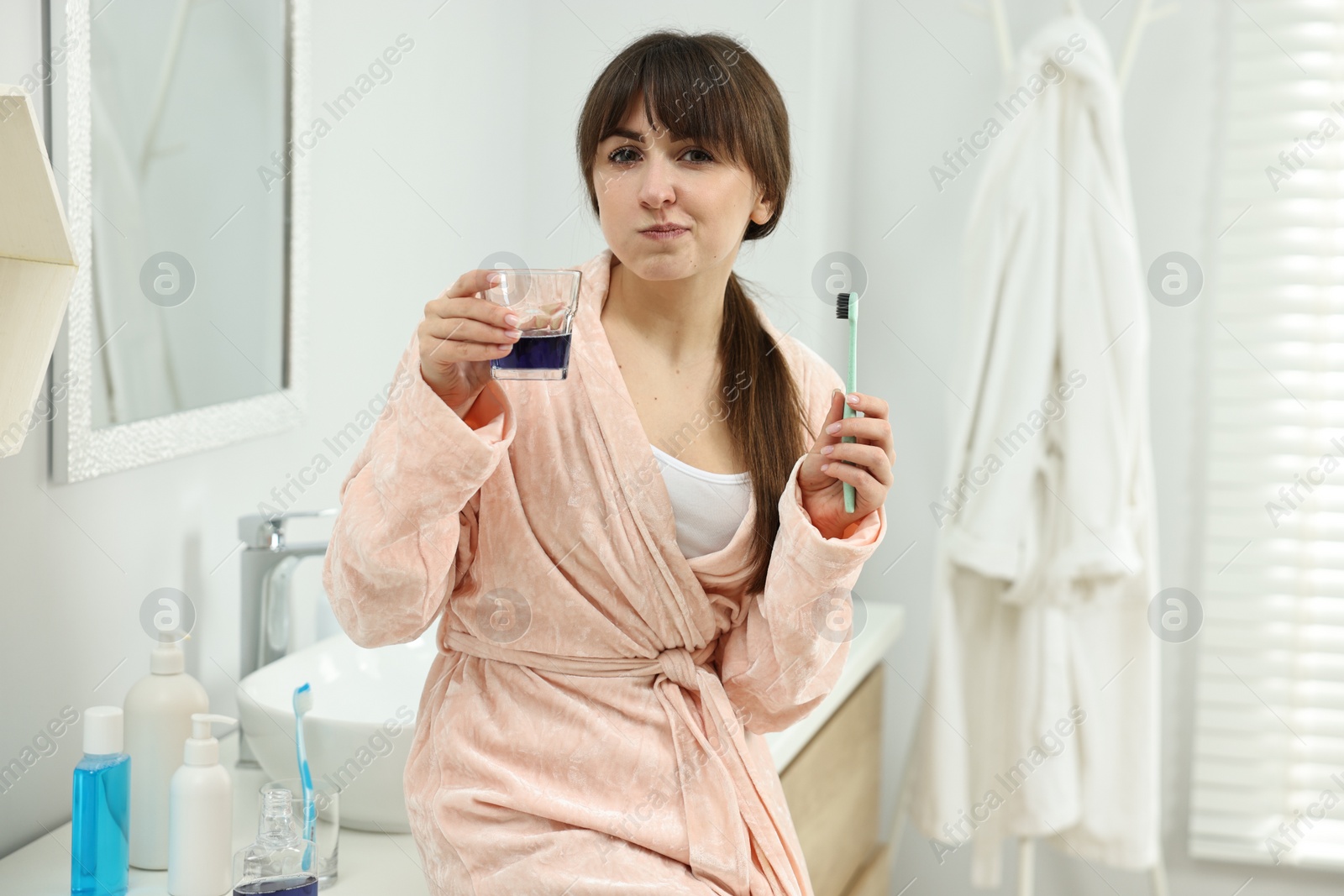 Photo of Young woman using mouthwash in bathroom. Oral hygiene