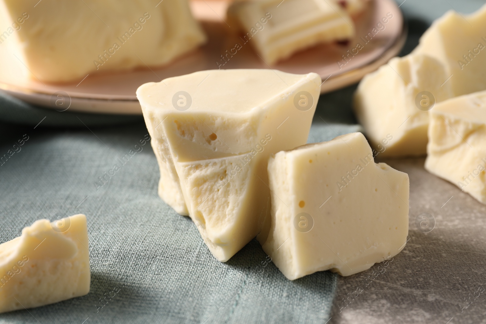 Photo of Pieces of tasty white chocolate on grey table, closeup