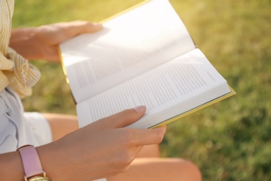 Young woman reading book outdoors on sunny day, closeup