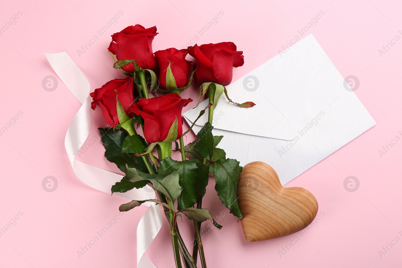 Photo of Flat lay composition with beautiful red roses and envelope on pink background. Valentine's Day celebration