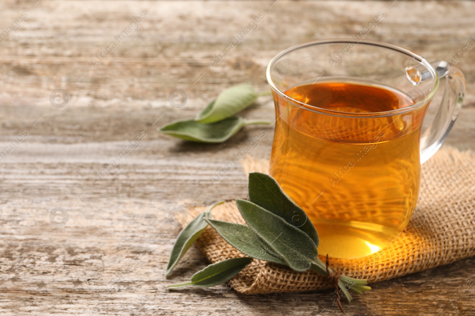 Photo of Cup of aromatic sage tea and fresh leaves on wooden table. Space for text