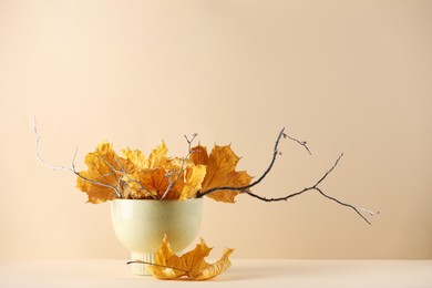 Photo of Beautiful autumn leaves and tree branches in vase on table against beige background, space for text