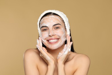 Happy young woman washing face with cosmetic product on beige background