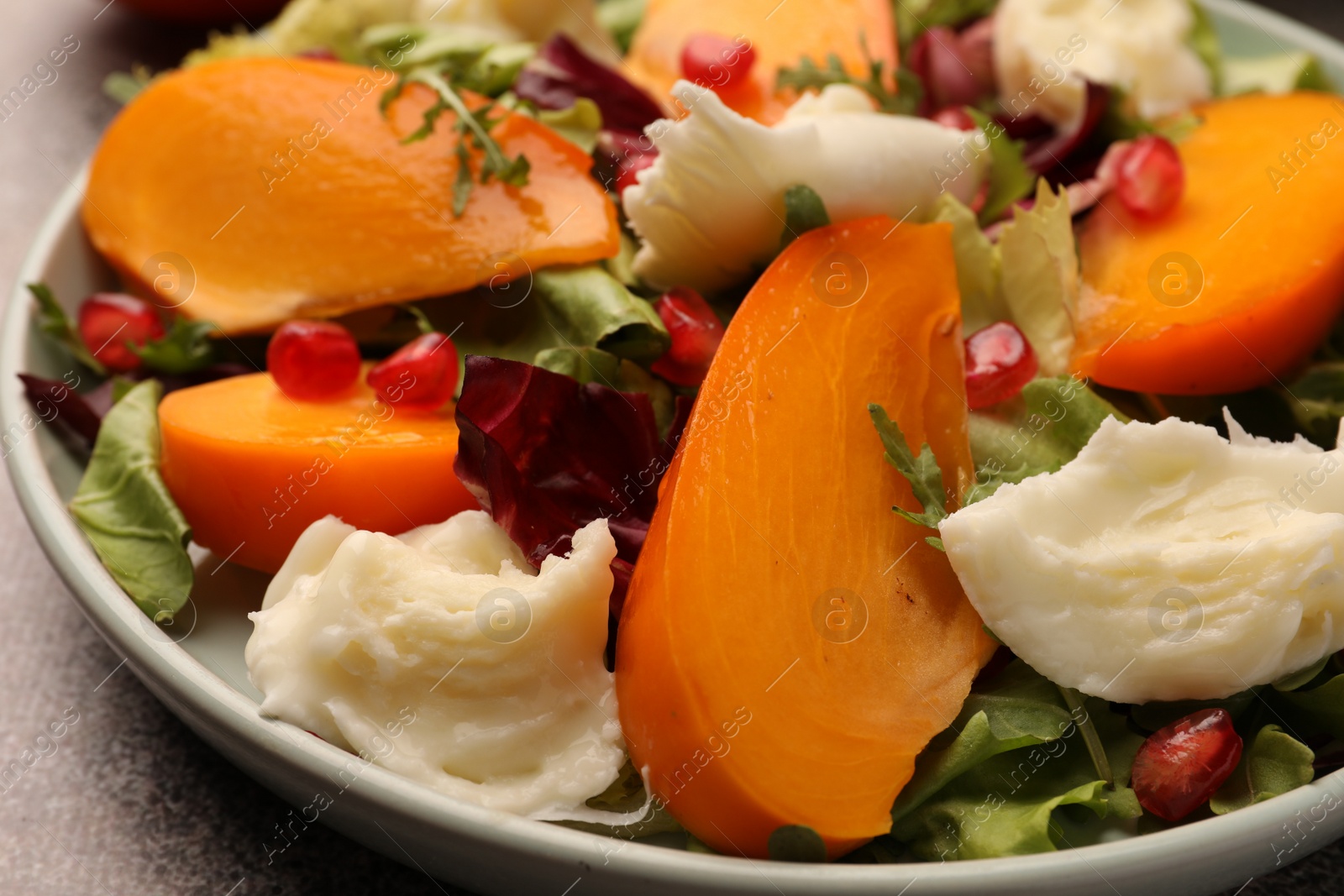 Photo of Delicious persimmon salad with cheese and pomegranate on grey table, closeup