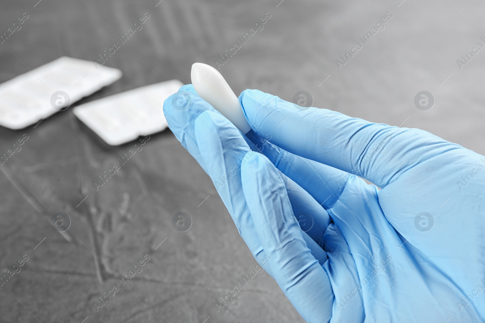 Photo of Woman holding suppository at grey table, closeup. Hemorrhoid treatment