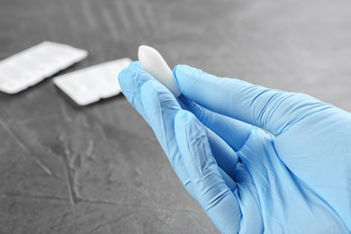 Photo of Woman holding suppository at grey table, closeup. Hemorrhoid treatment