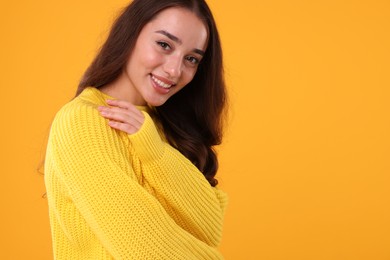 Photo of Beautiful young woman in stylish warm sweater on orange background, space for text