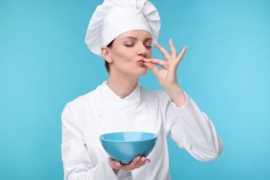 Woman chef in uniform holding bowl and showing perfect sign on light blue background