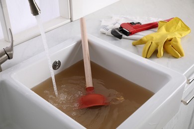 Kitchen counter with clogged sink, plunger and plumber's accessories