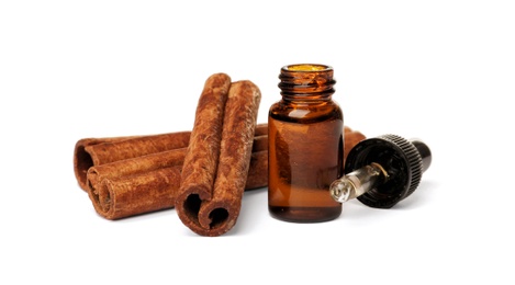 Photo of Bottle of cinnamon oil, dropper and sticks on white background