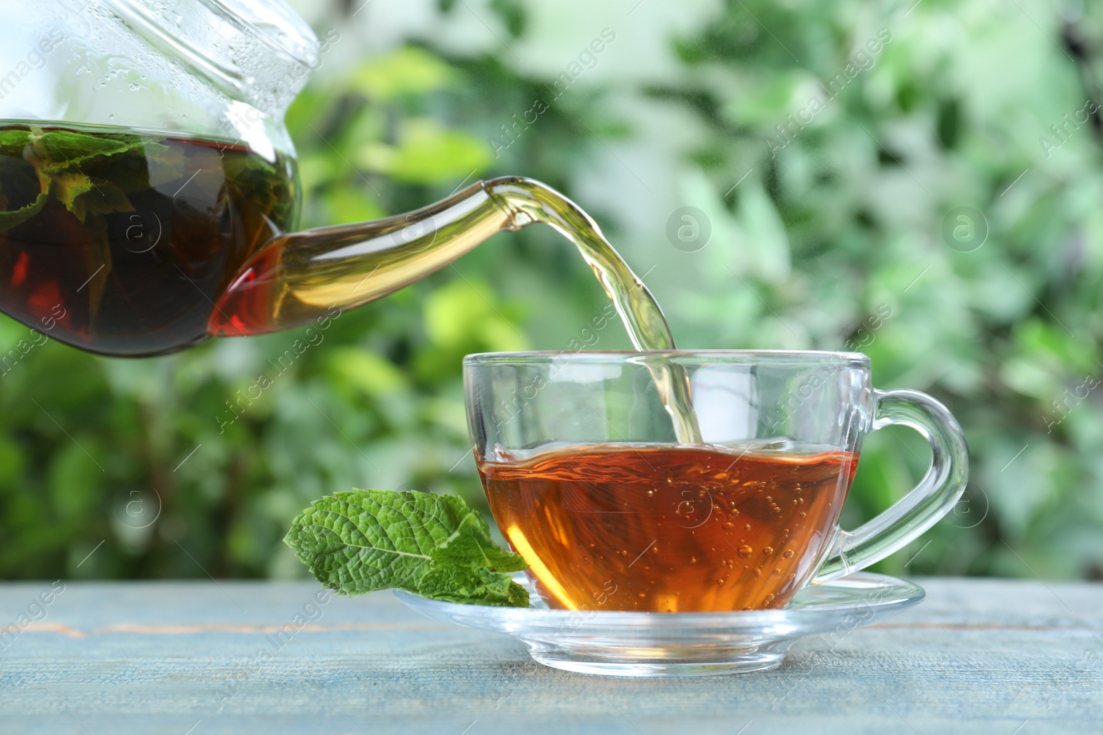 Photo of Pouring fresh mint tea into cup on blue wooden table, closeup