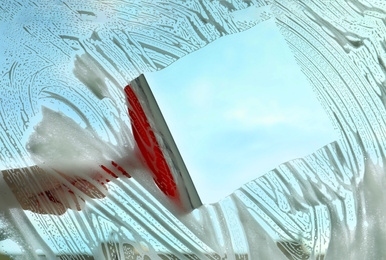 Photo of Woman cleaning window with squeegee on spring day, closeup