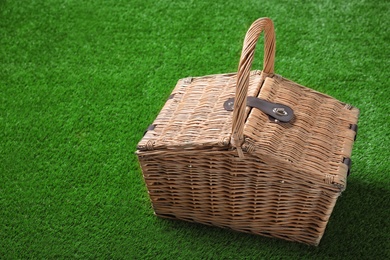 Photo of Closed wicker picnic basket on green grass, space for text