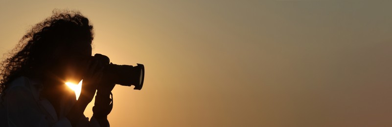 Image of Photographer taking photo with professional camera outdoors at sunset, space for text. Banner design