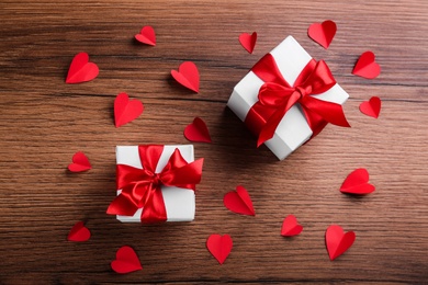 Photo of Beautiful gift boxes and paper hearts on wooden table, flat lay. Valentine's Day celebration