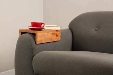 Cup of tea and book on sofa with wooden armrest table in room. Interior element