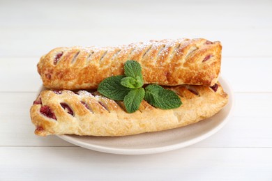 Fresh tasty puff pastry with sugar powder and mint on white wooden table, closeup