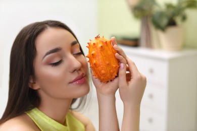 Young woman with fresh kiwano at home, space for text. Exotic fruit