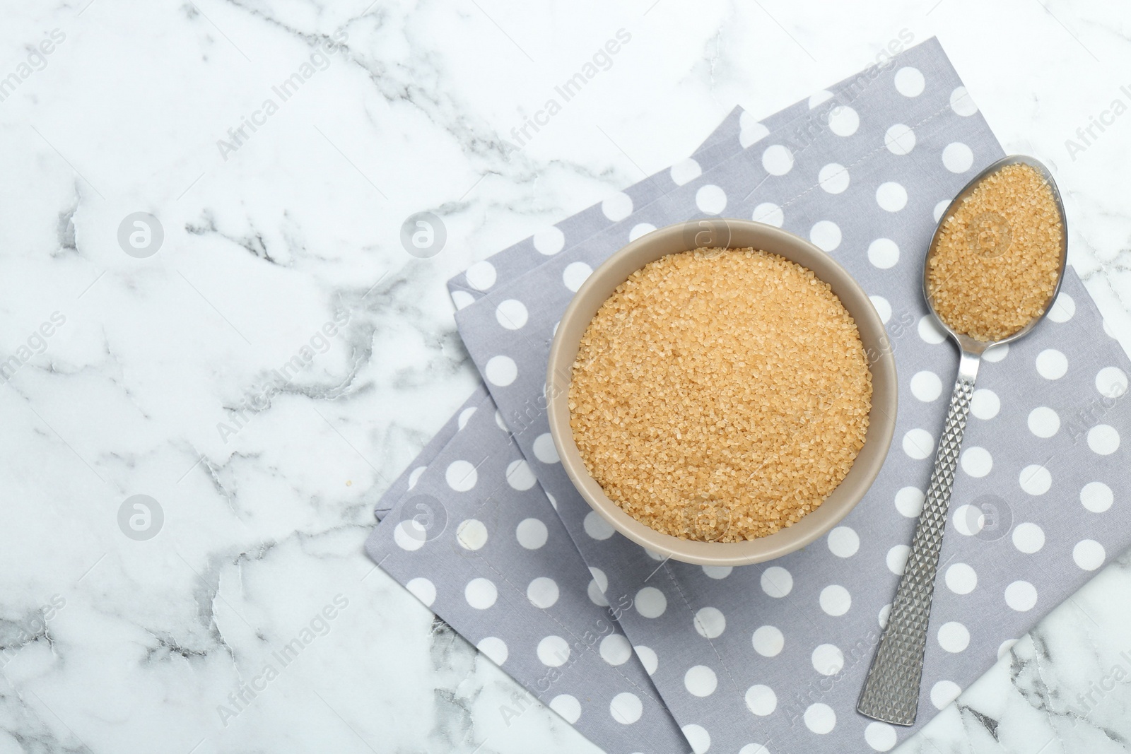 Photo of Brown sugar in bowl and spoon on white marble table, top view. Space for text