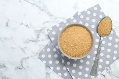 Photo of Brown sugar in bowl and spoon on white marble table, top view. Space for text