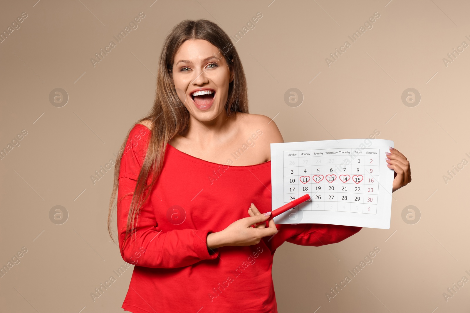 Photo of Young woman holding calendar with marked menstrual cycle days on beige background