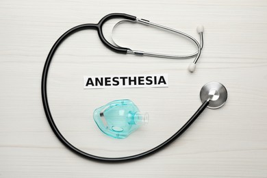 Word Anesthesia, mask and stethoscope on white wooden table, flat lay