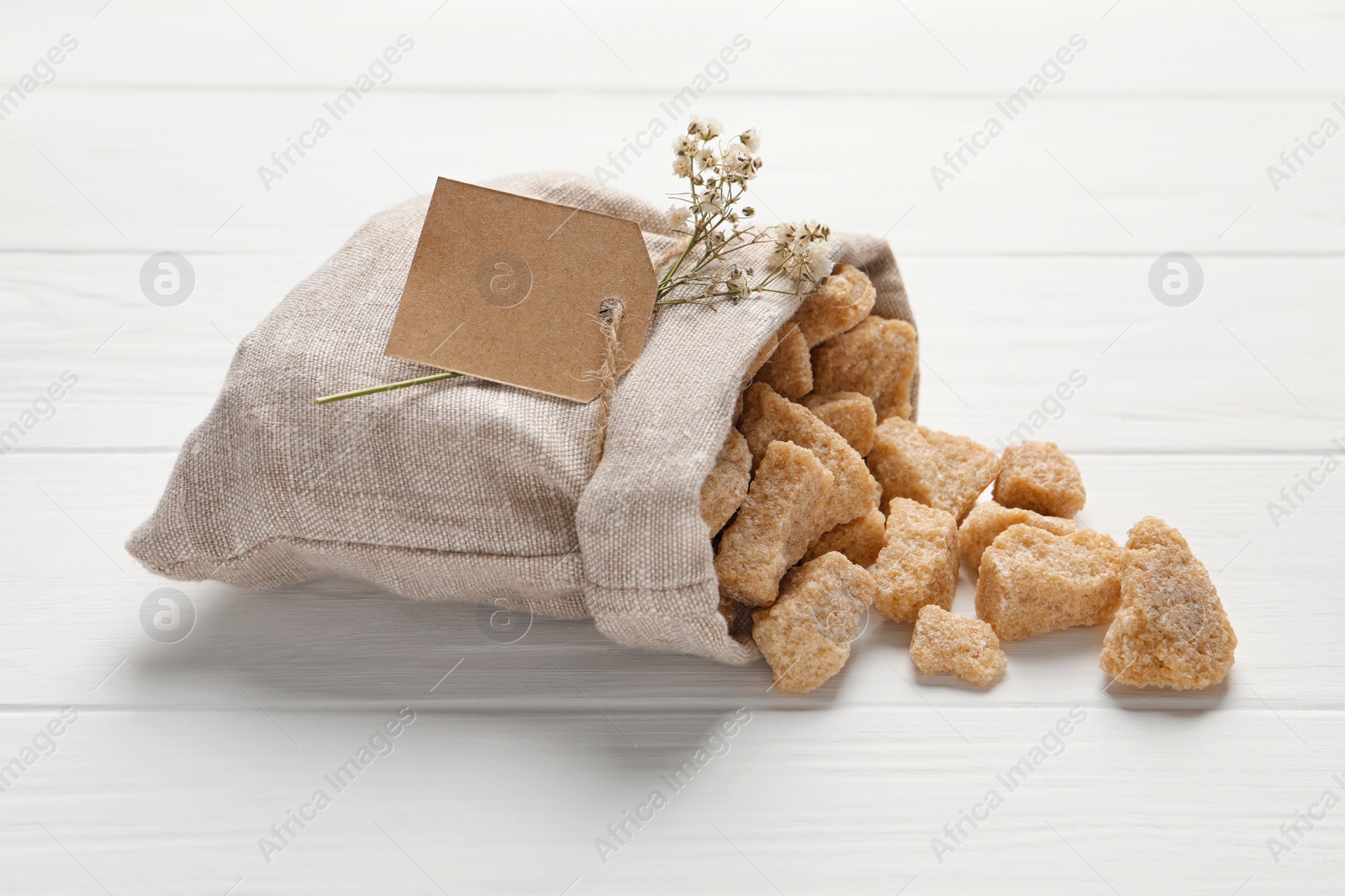 Photo of Bag of brown sugar pieces on white wooden table