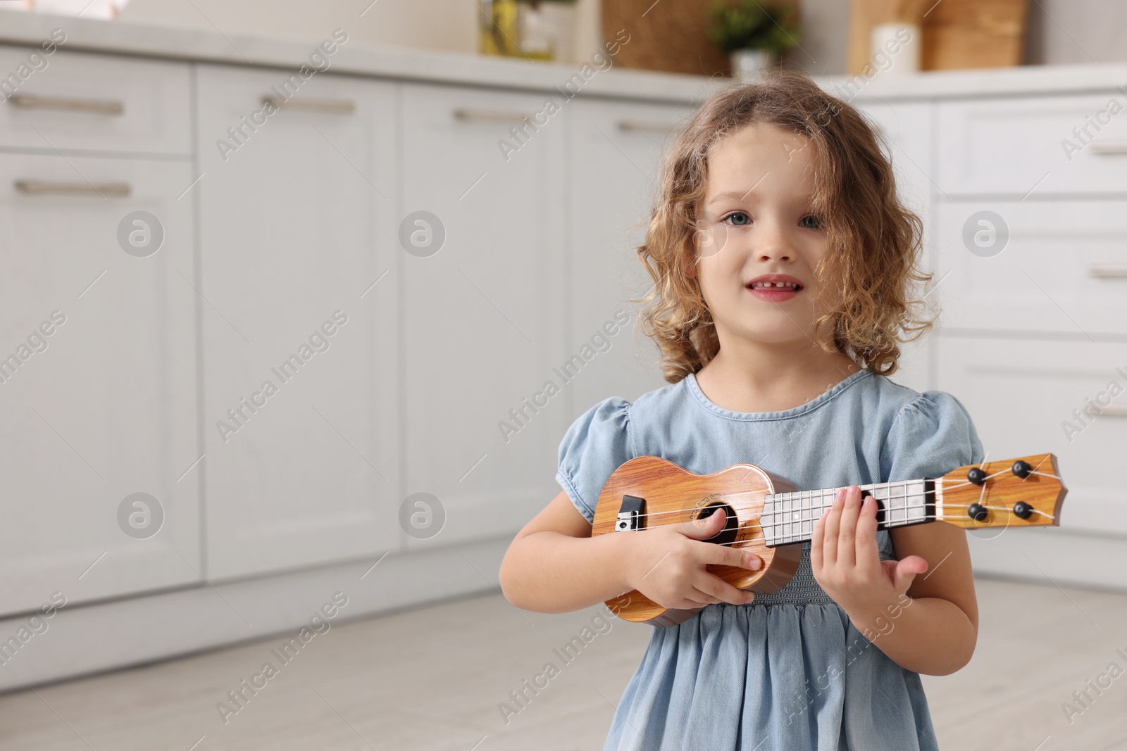 Photo of Little girl playing toy guitar in kitchen. Space for text